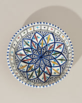 A ceramic hand painted decorative plate with a geometric pattern, predominantly white with blue and gold accents.